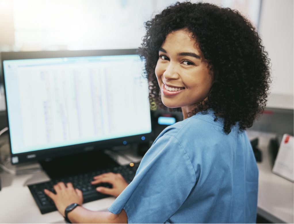 A smiling GP practice administrator at her computer